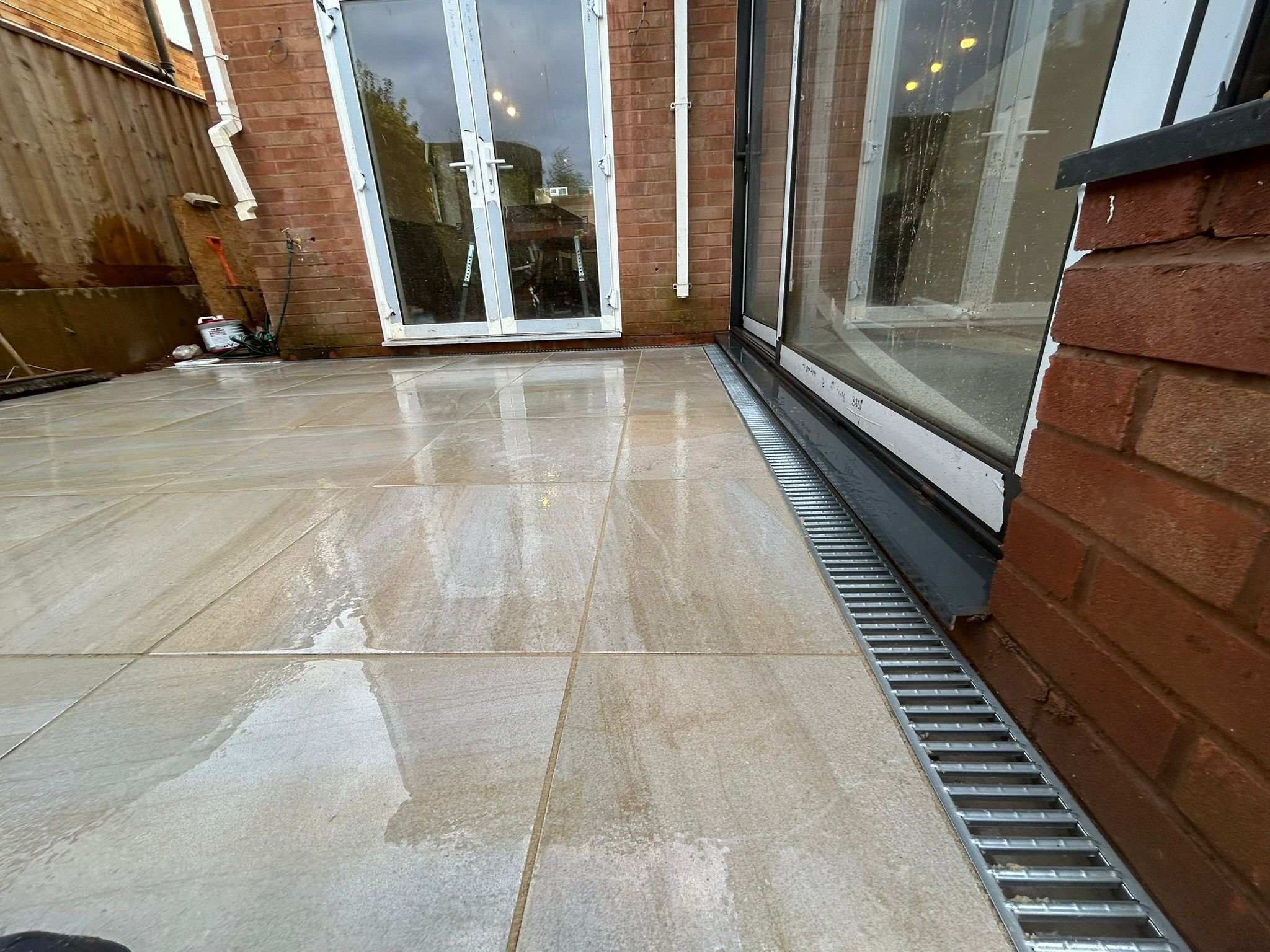 Wet-look porcelain patio laid by R A Groundworks at bifold doors with brick wall and drainage channel